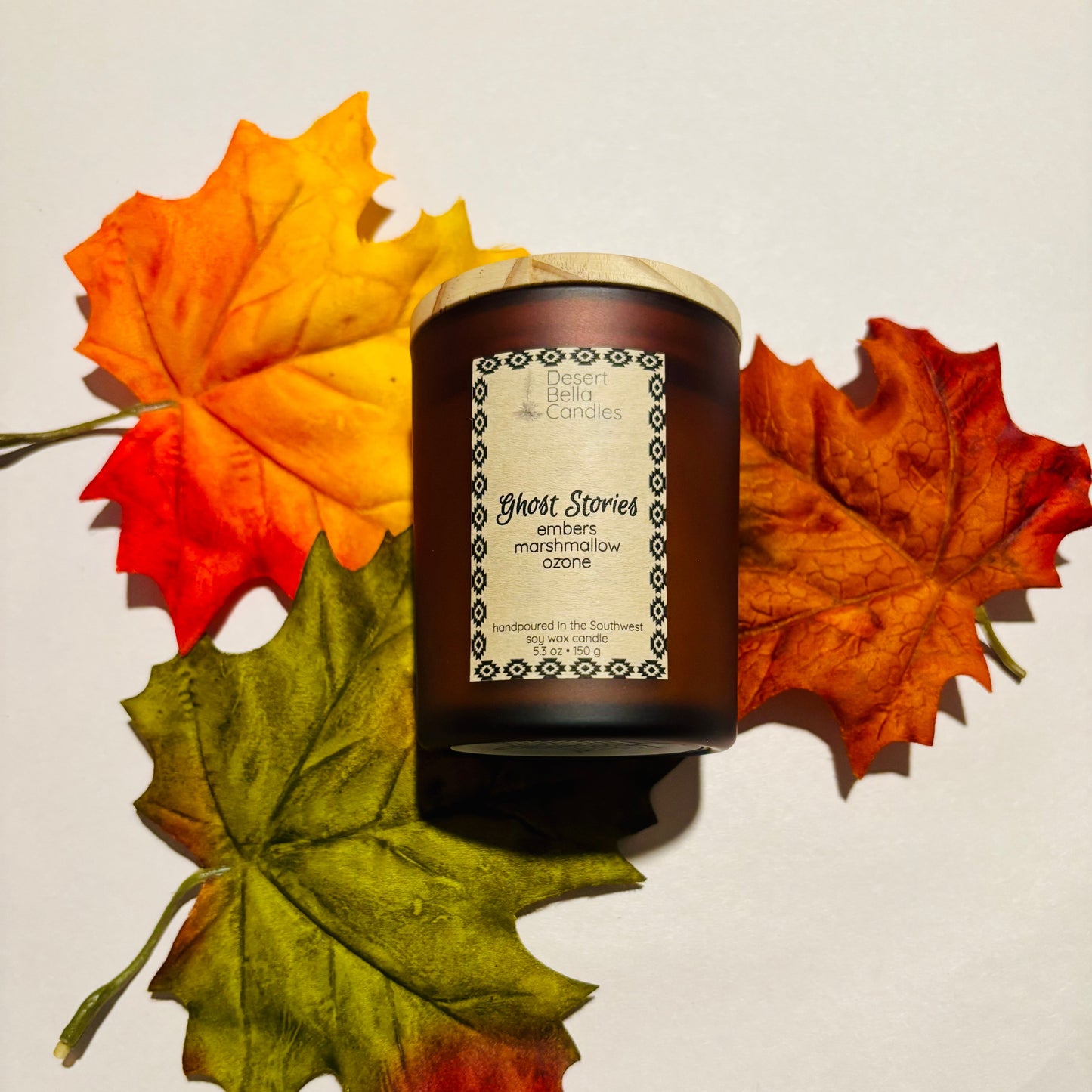 Candle labeled 'Ghost Stories' with autumn leaves on a light background