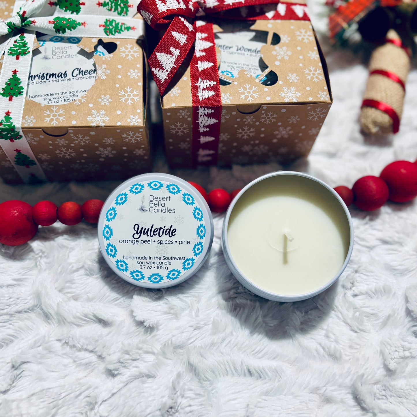 Candle in a tin with a Christmas-themed gift box and decorative beads on a white surface
